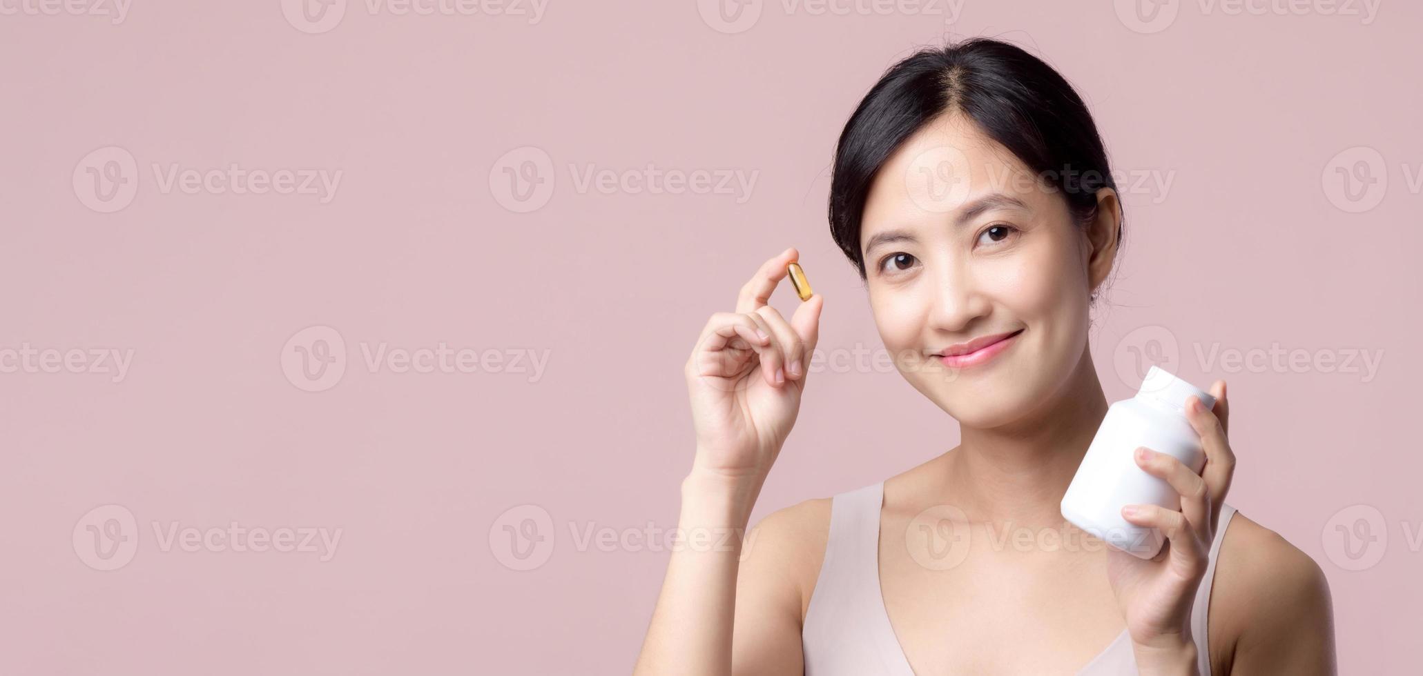 portret jong Aziatisch vrouw gelukkig glimlach gezicht met vitamine voeding pil. mooi schattig meisje vrouw persoon Holding Gezondheid capsule supplement huid zorg geïsoleerd Aan roze achtergrond. geneesmiddel concept. foto