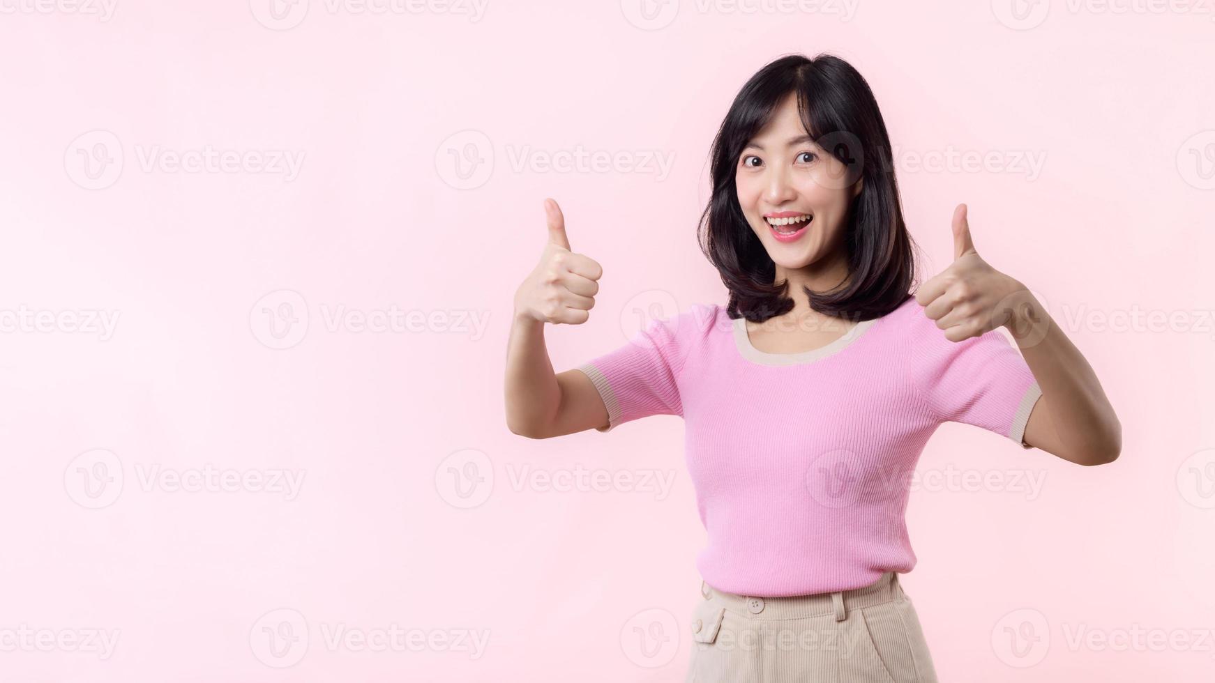 portret jong gelukkig Aziatisch vrouw vrolijk glimlach tonen duim omhoog, vertrouwen, adviseren gebaar geïsoleerd Aan roze pastel studio achtergrond. mooi aantrekkelijk vrouw met Leuk vinden hand- teken. levensstijl meisje vrouw foto