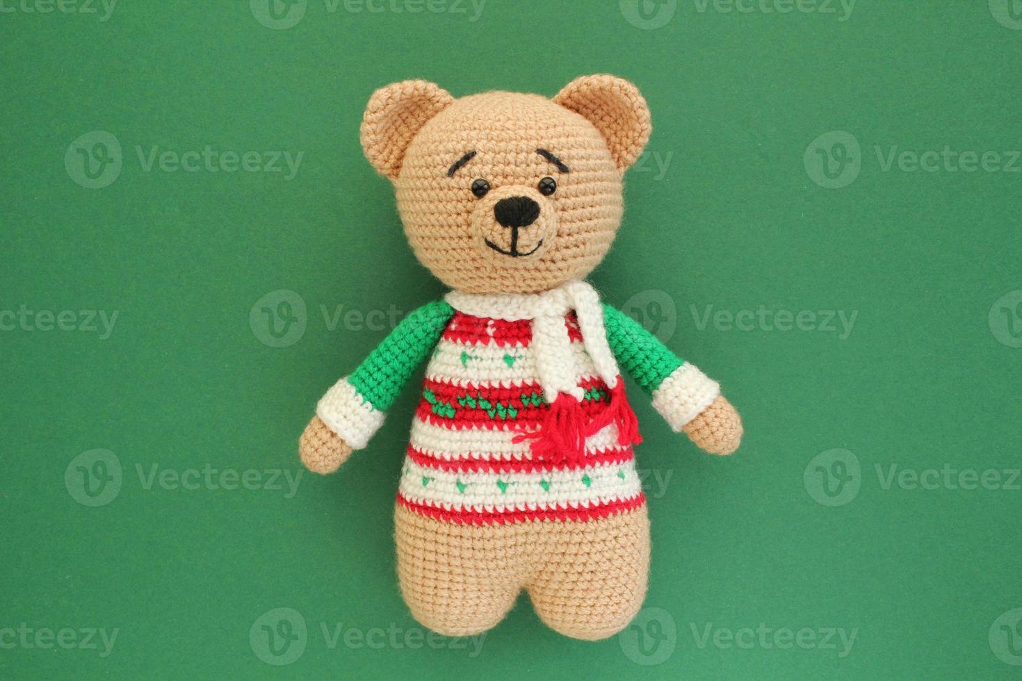 haken amigurumi handgemaakt gevuld zacht teddy beer speelgoed- in gekleurde trui Aan groen achtergrond. handwerk, hobby. ambacht diy pasgeboren zwangerschap concept. gebreid pop voor weinig baby. detailopname vlak leggen uit foto