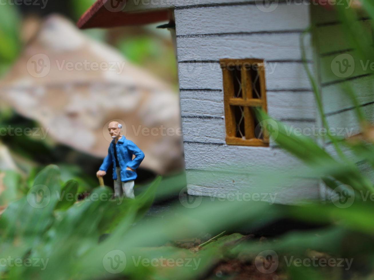 een dichtbij omhoog van een miniatuur figuur van een oud Mens aan het wachten in voorkant van de huis. foto