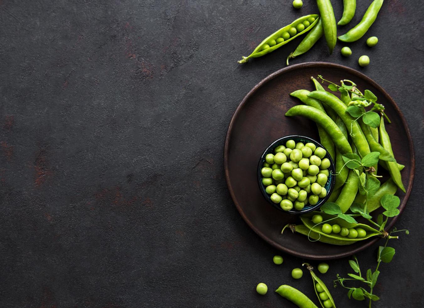 groene erwten in een kom met verse peulen op de zwarte betonnen achtergrond foto