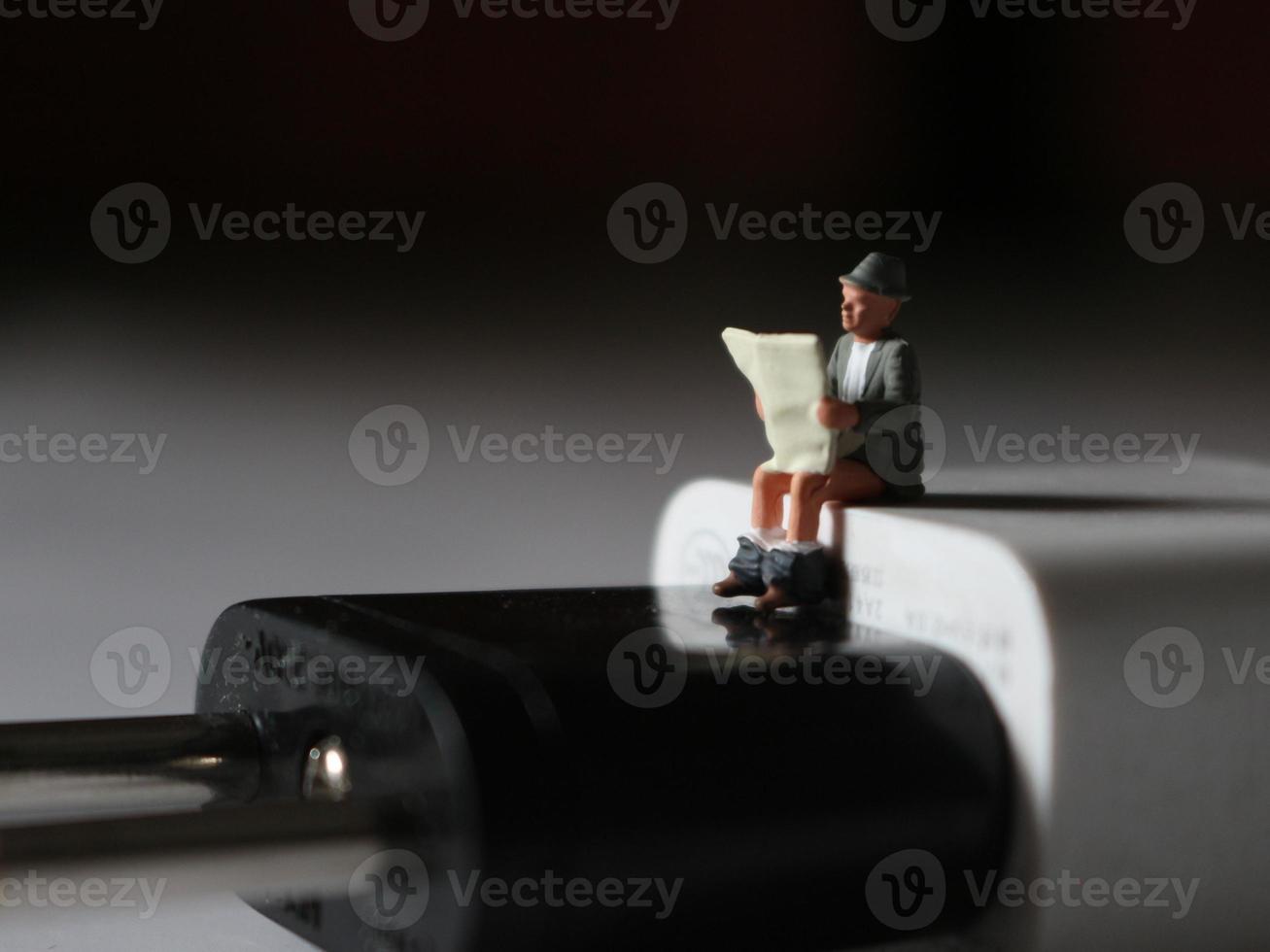 een dichtbij omhoog van een miniatuur figuur van een persoon lezing bovenstaand een cel telefoon oplader. foto