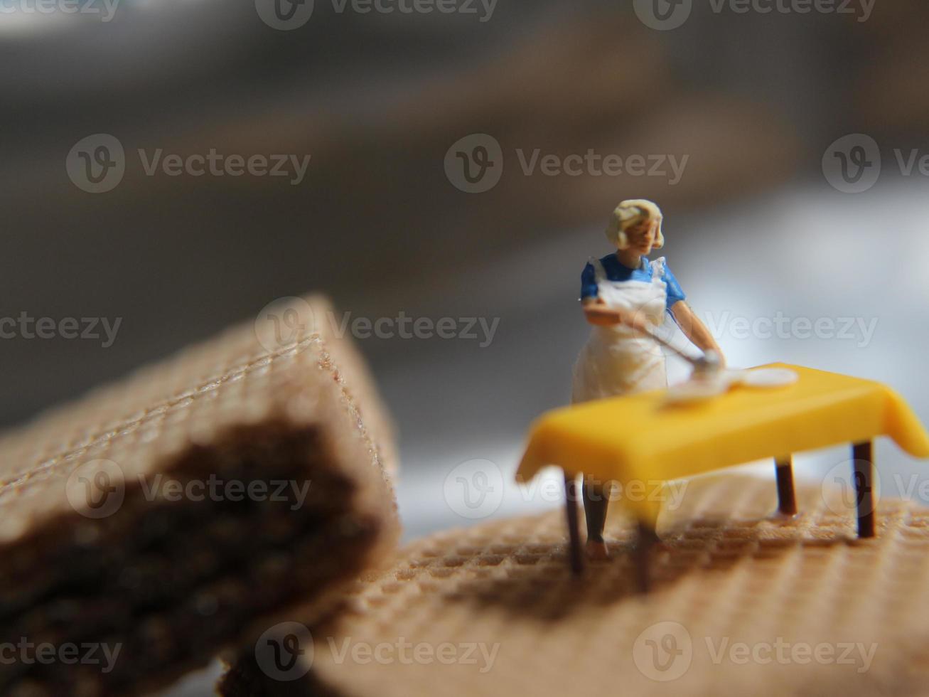 een miniatuur figuur van een vrouw Koken Aan een chocola wafeltje. foto