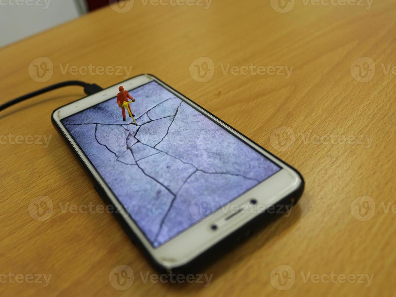 een miniatuur figuur van een snelweg arbeider breken een cel telefoon scherm. foto