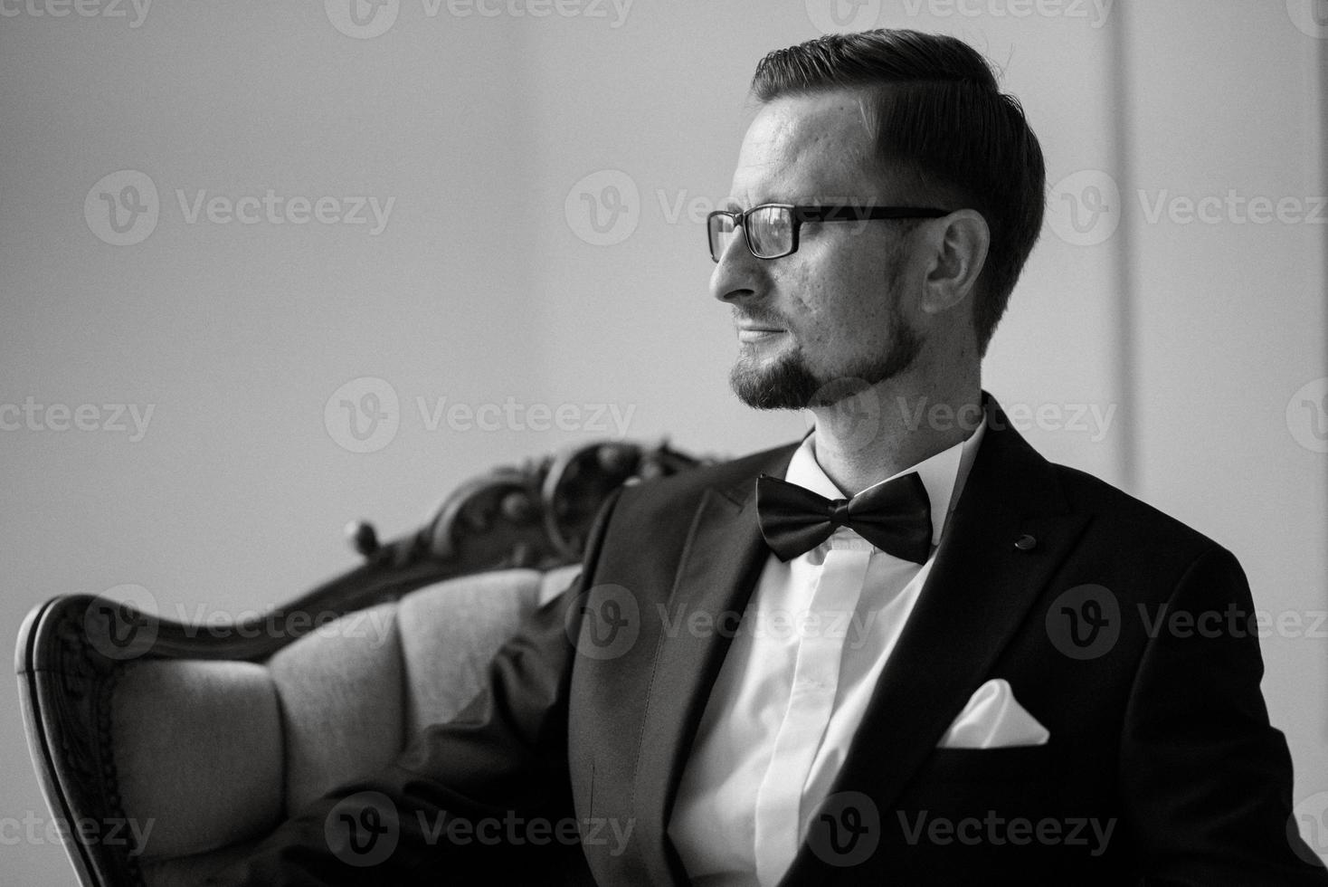 portret van een bruidegom in een zwart pak en bril in een studio foto