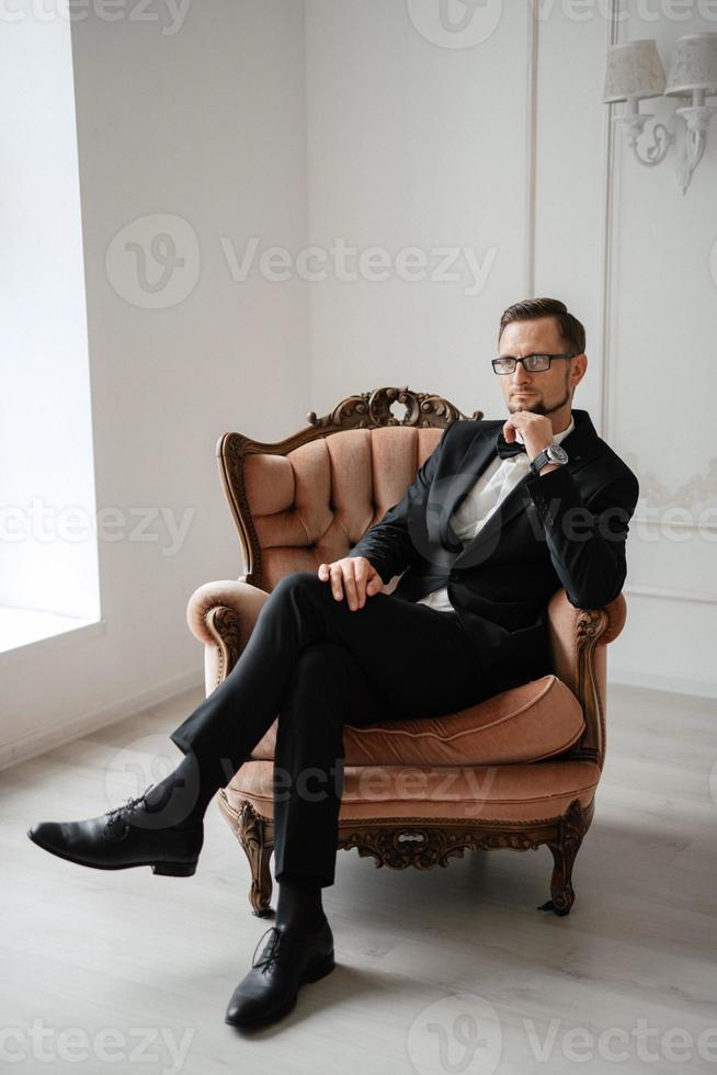 portret van een bruidegom in een zwart pak en bril in een studio foto