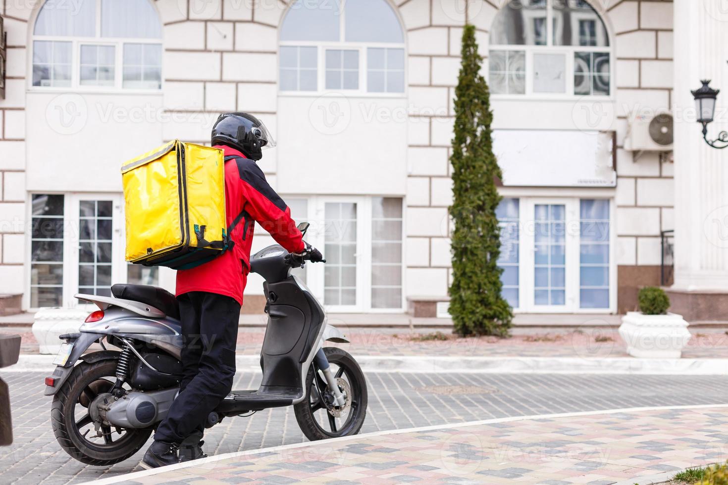 geel levering doos Aan motorfiets met levering Mens in voorkant van huis. foto