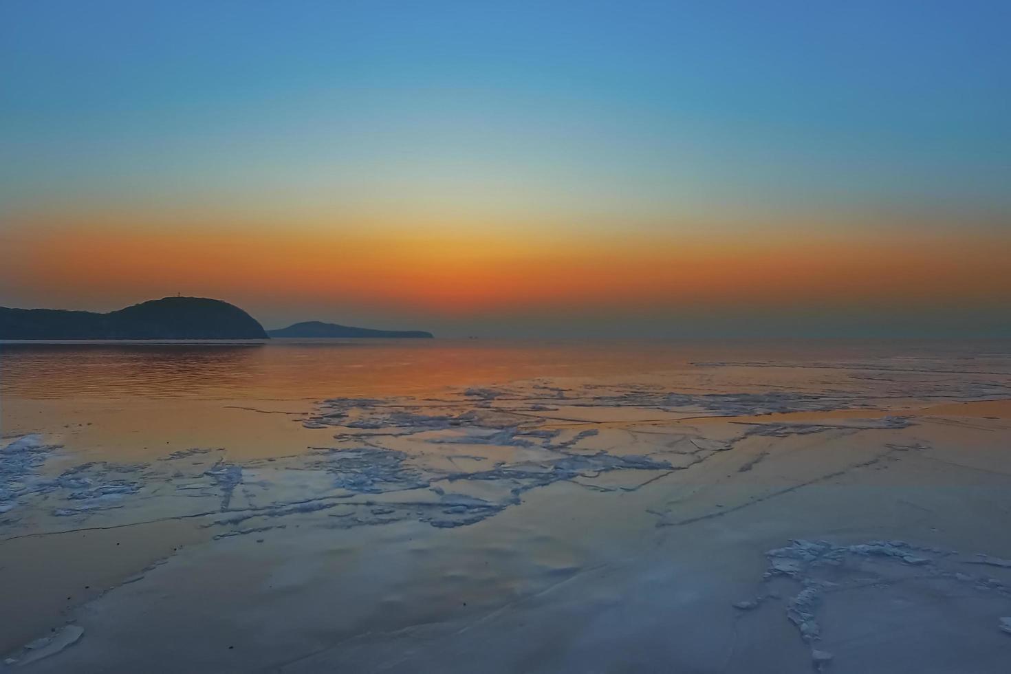 zeegezicht met kleurrijke oranje zonsondergang en bergen met ijsschotsen in de zee in Vladivostok, Rusland foto