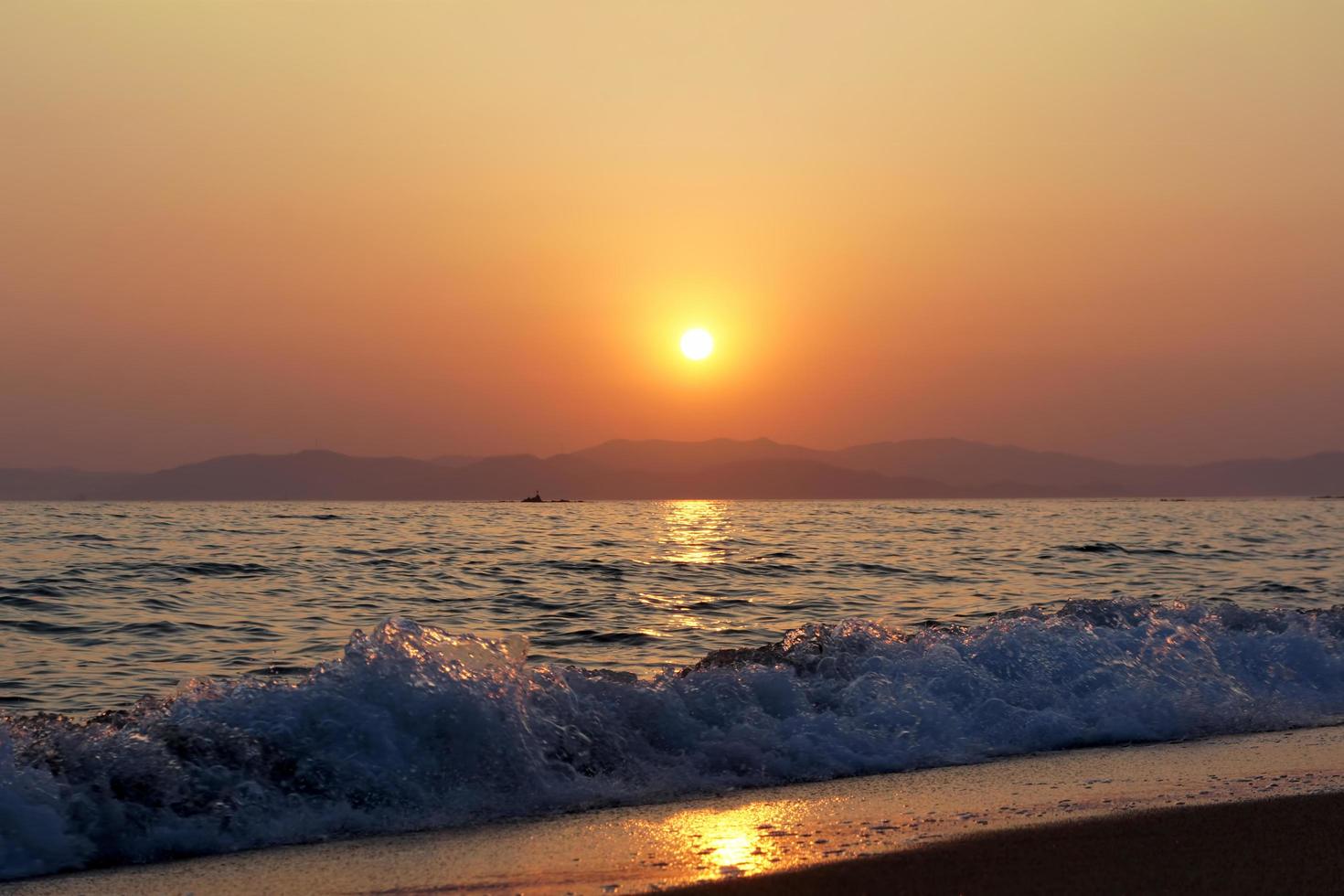 golven die breken op een strand met oranje bewolkte zonsondergang over bergen foto