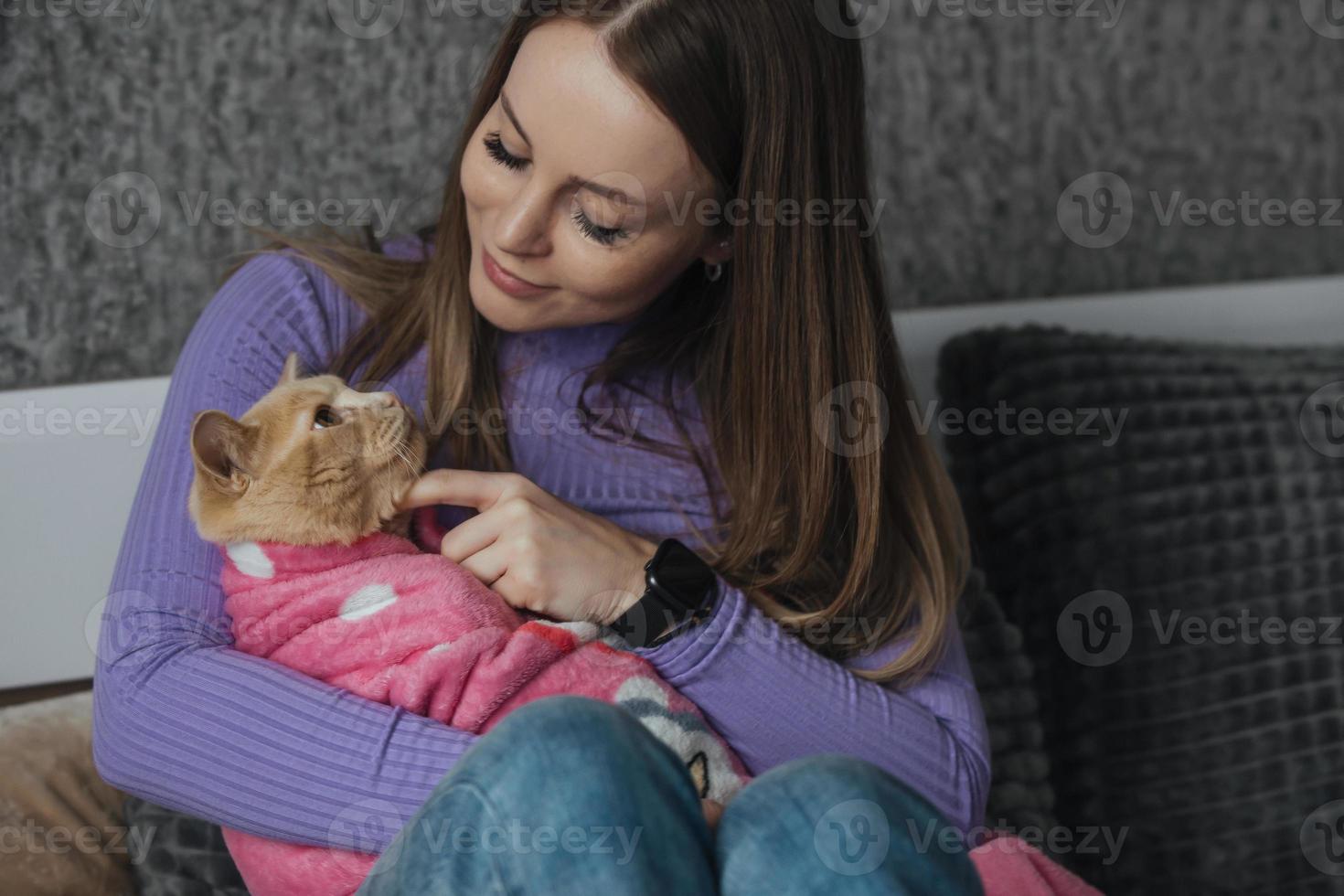 een jong vrouw in haar slaapkamer houdt haar huisdier kat verpakt in een baby deken in haar armen. liefde en zorg voor dieren, kinderloos vrouw. behandelen dieren Leuk vinden uw kinderen foto