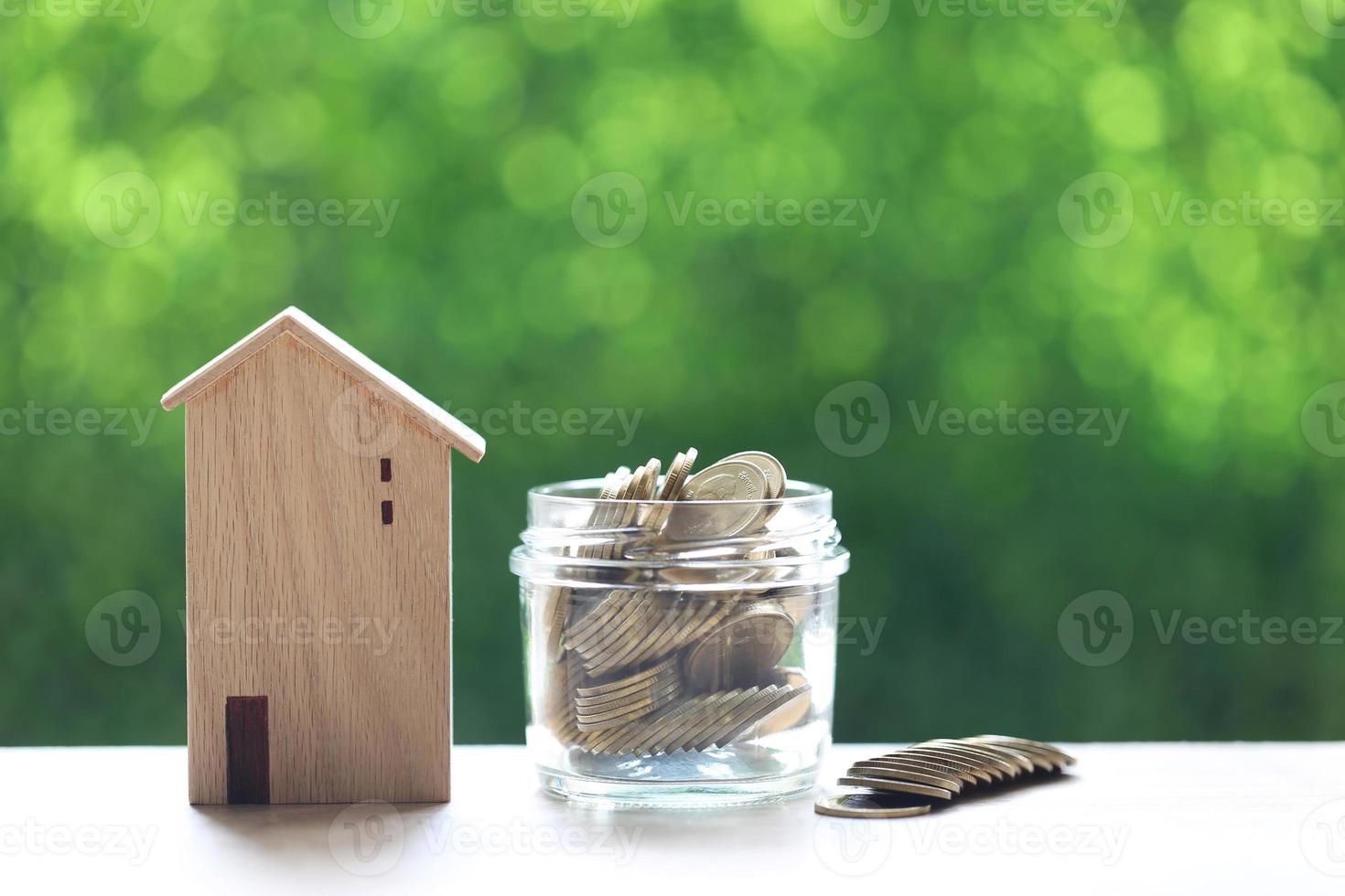 modelwoning met stapels munten op een natuurlijke groene achtergrond, geld besparen voor de voorbereiding van de toekomst en investeringsconcept foto