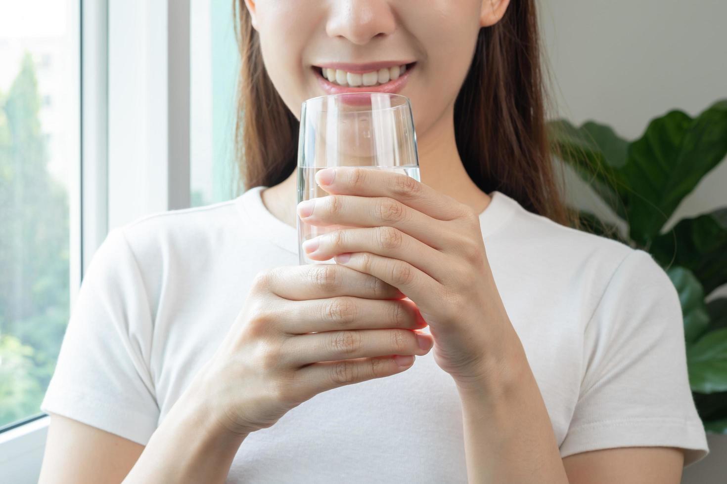 gelukkig mooi, Aziatisch jong vrouw, meisje drinken, slokje vers glas van water voor hydratatie van lichaam, Holding transparant glas in haar hand, dorstig Bij huis. Gezondheid zorg, gezond levensstijl concept. foto