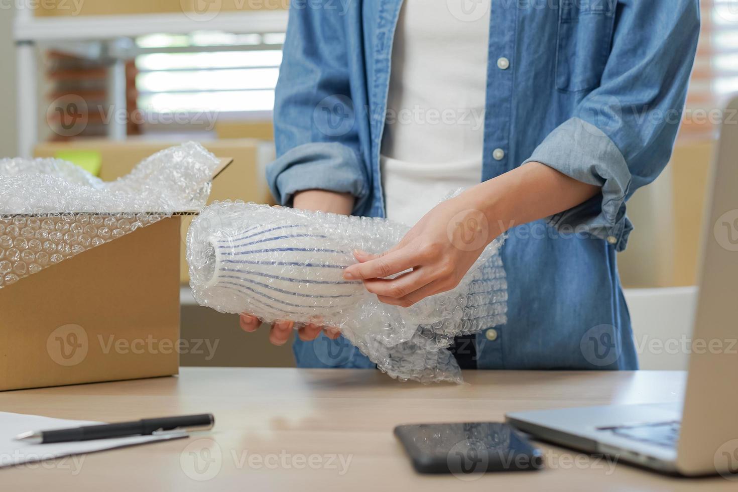 klein bedrijf ondernemer MKB, Aziatisch jong vrouw eigenaar inpakken Product, controle pakket doos levering, gebruik makend van laptop te ontvangen bestellen van klant, werken Bij huis kantoor. handelaar online, e-commerce. foto