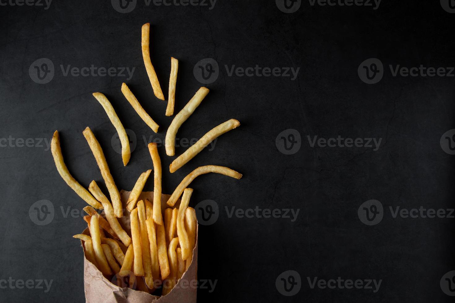 hete knapperige frietjes in een papieren zak op zwarte achtergrond. lekker Amerikaans fastfood. foto