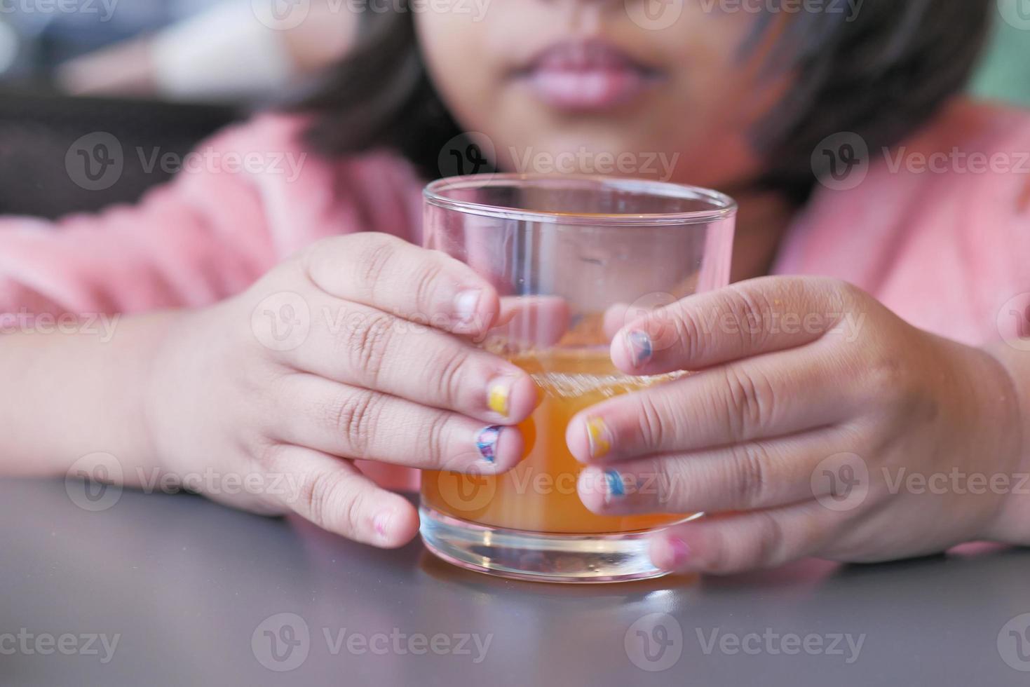 kind Holding een glas van oranje sap dichtbij omhoog foto