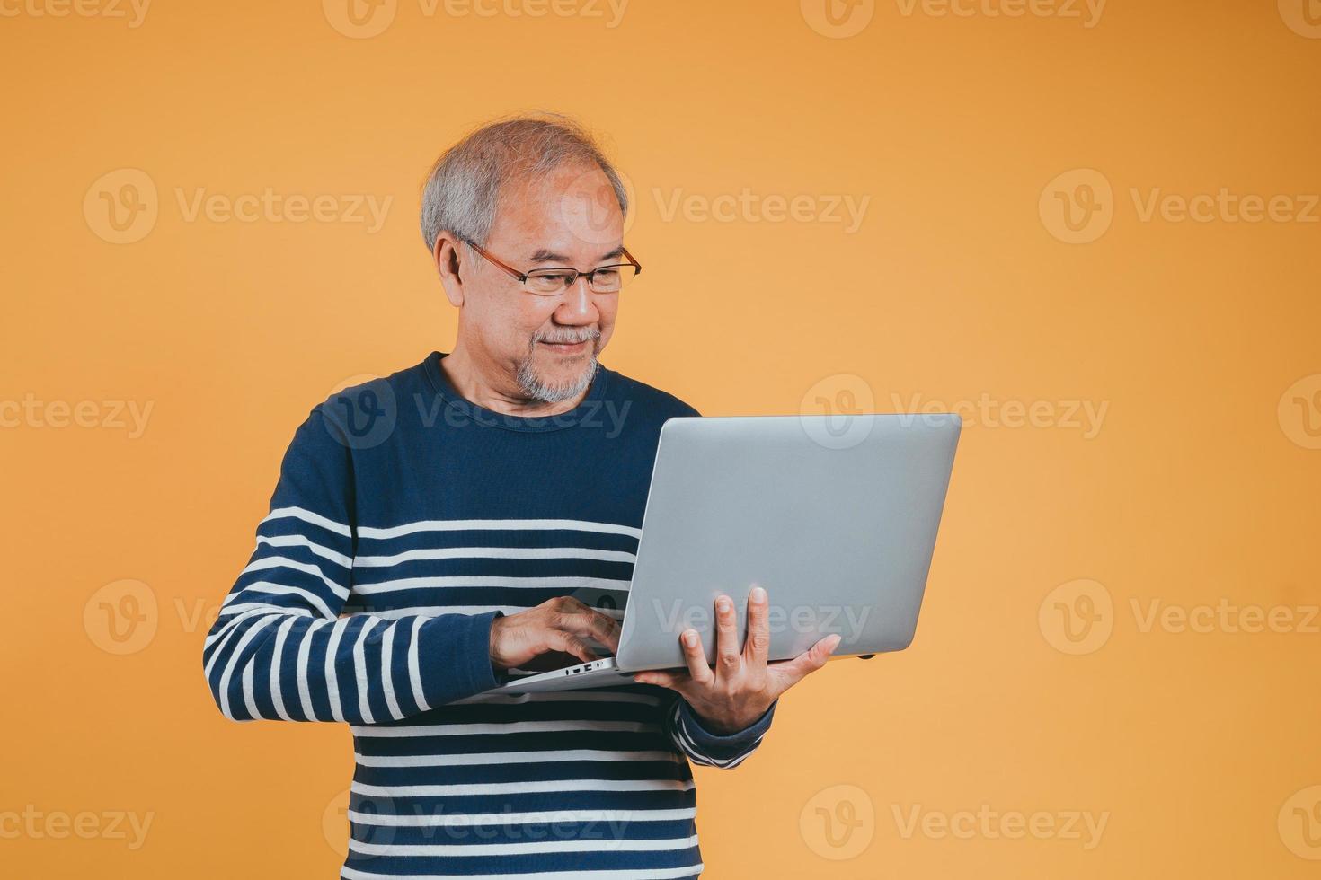 Aziatisch senior Mens gebruik makend van laptop computer voor werken na pensioen Aan de geel achtergrond. foto