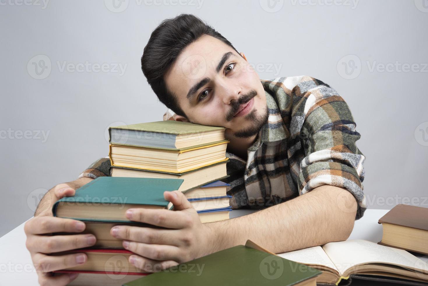 een jonge mannelijke student zit met veel boeken en bereidt zich voor op de klas foto