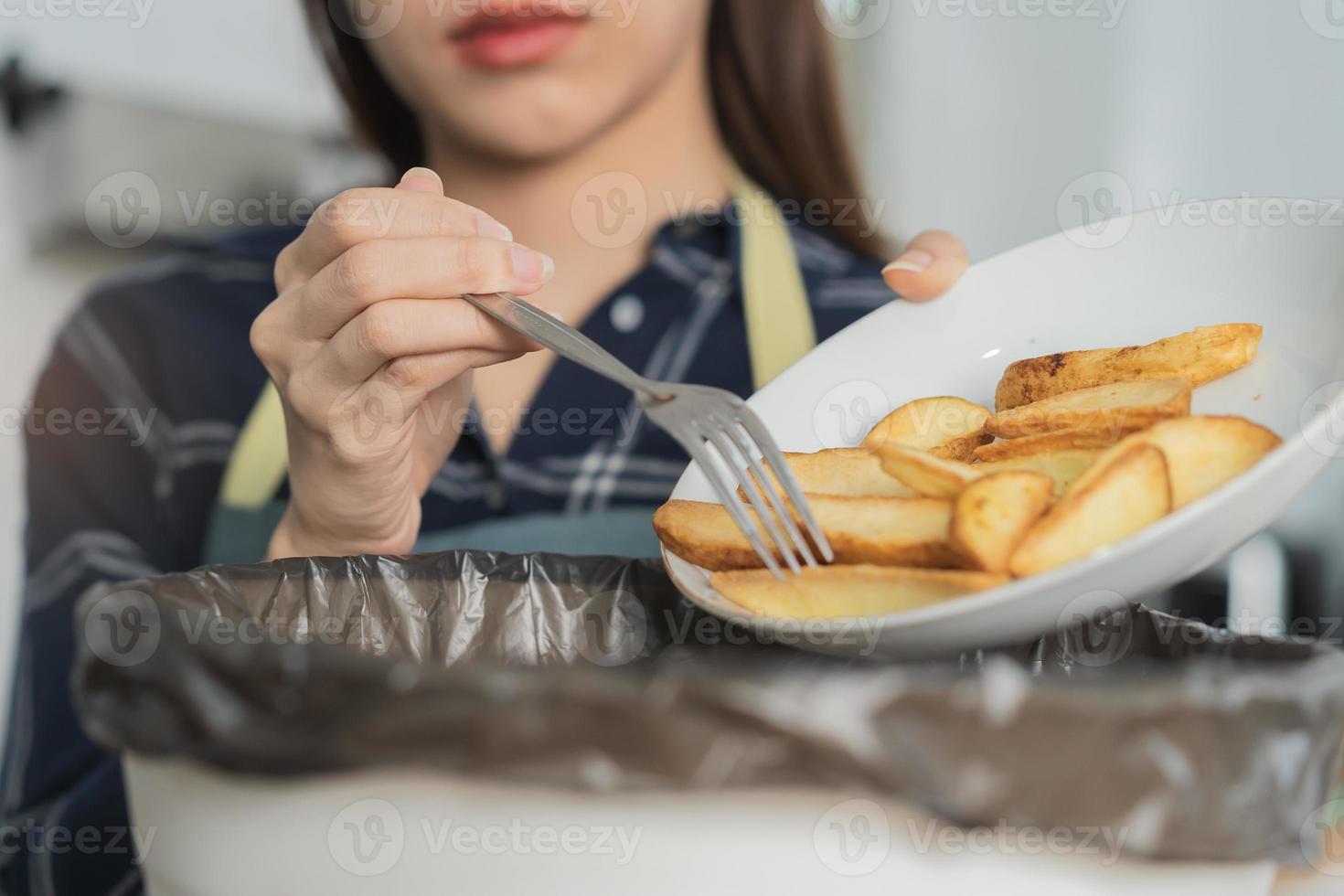 cholesterol van rommel maaltijd is dik maaltijd, hand- van Aziatisch jong huishouden vrouw schrapen, het werpen voedsel restjes in afval, uitschot bak van aardappel chip, tussendoortje. milieuvriendelijk aansprakelijk, ecologie foto