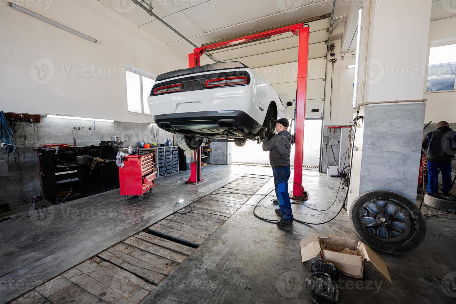 monteur in onderhoud reparatie station werken met spier auto, ontmantelt een wiel Aan tillen. foto