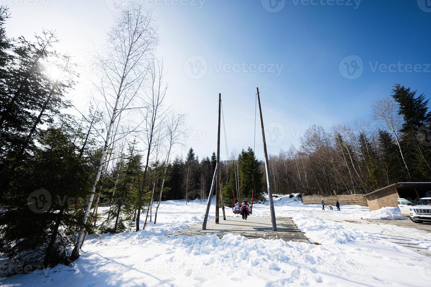 moeder swinging met dochters in groot houten schommel in vroeg voorjaar besneeuwd bergen. foto