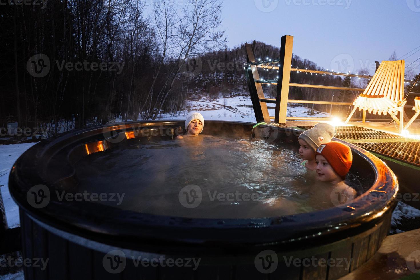 kinderen genieten van het baden in houten vat heet kuip in de terras van de huisje. Scandinavisch bad met een haard naar brandwond hout en warmte water. foto
