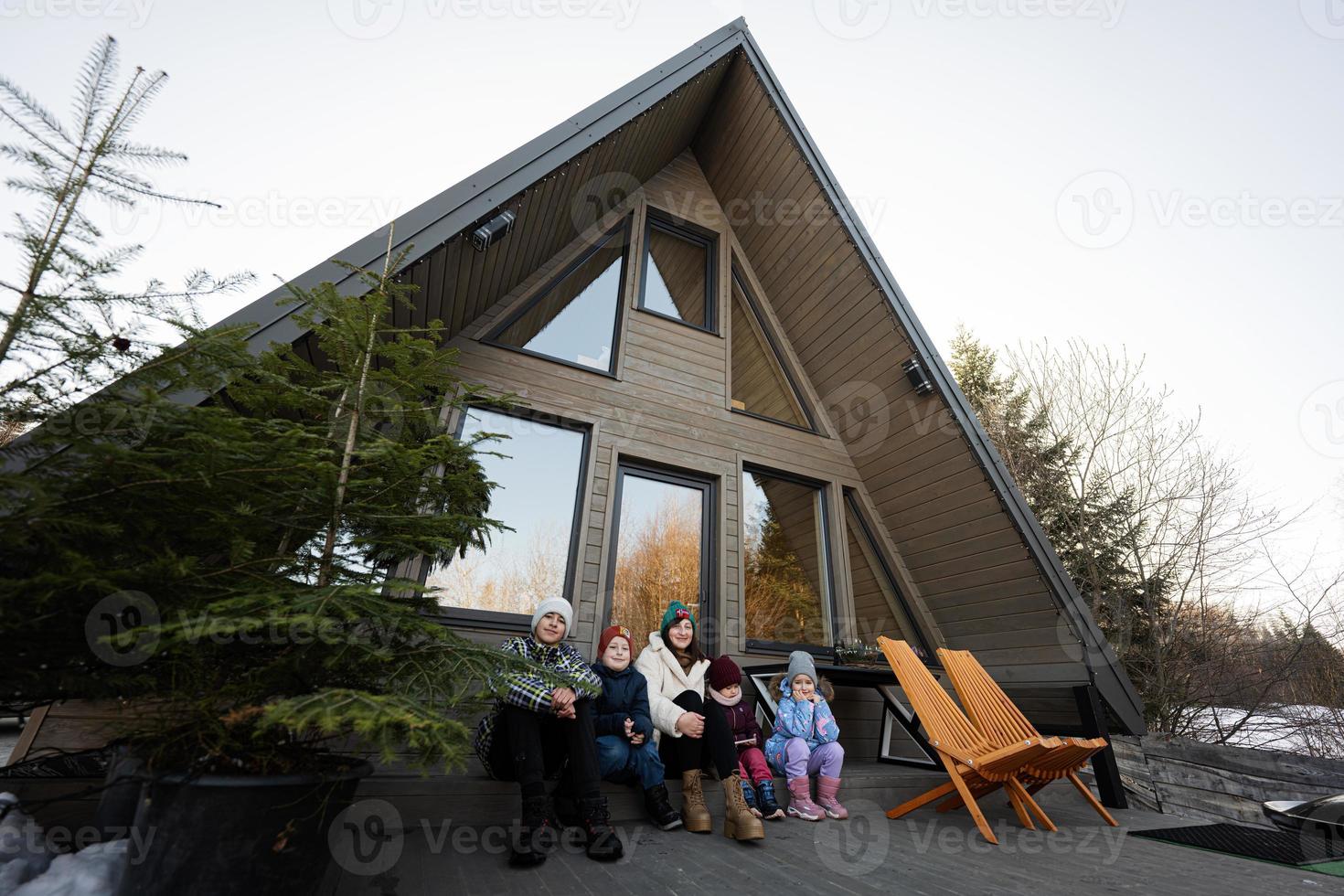 moeder met vier kinderen zitten Aan terras uit rooster klein huis in de bergen. foto