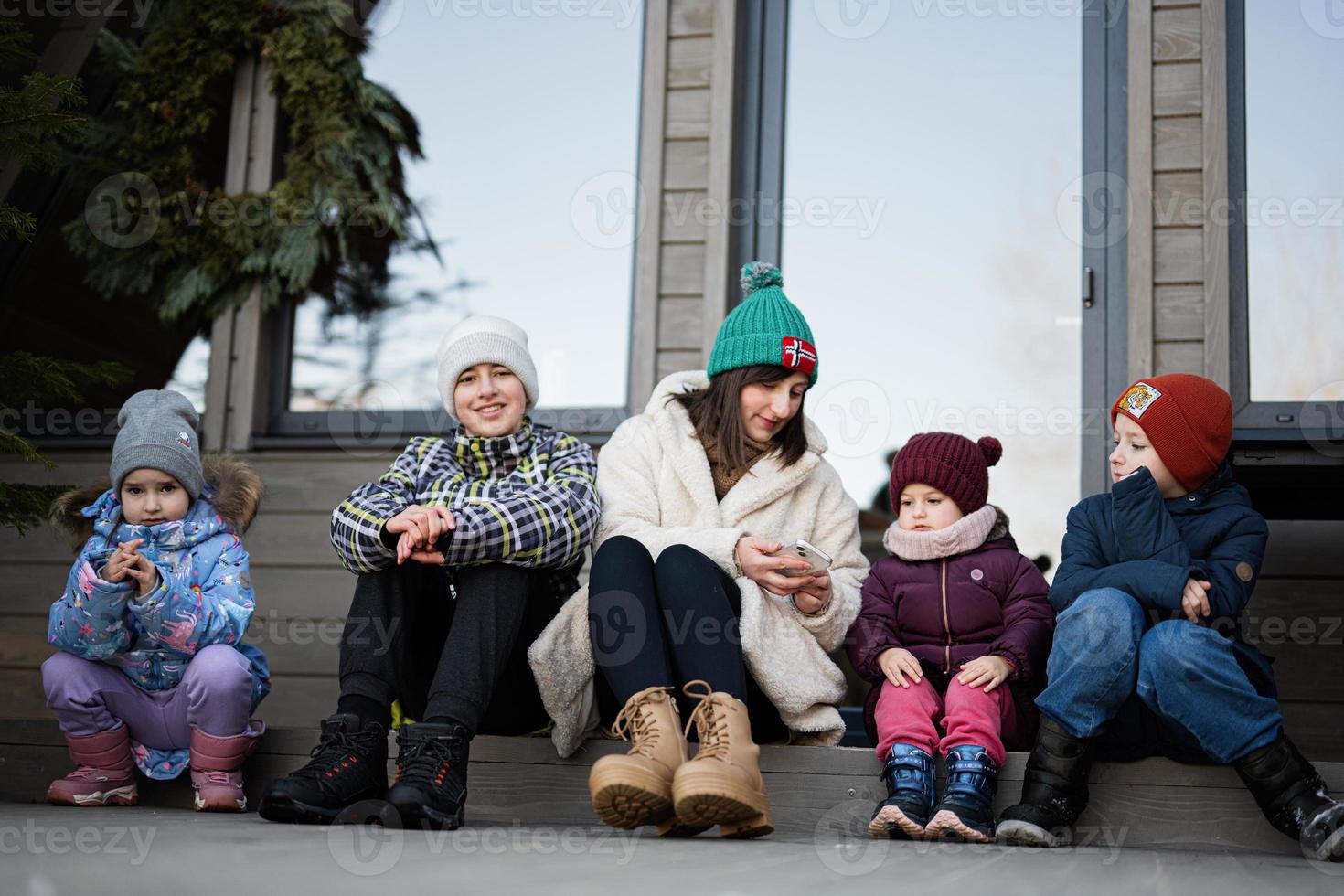 moeder met vier kinderen zitten Aan terras uit rooster klein huis in de bergen. foto