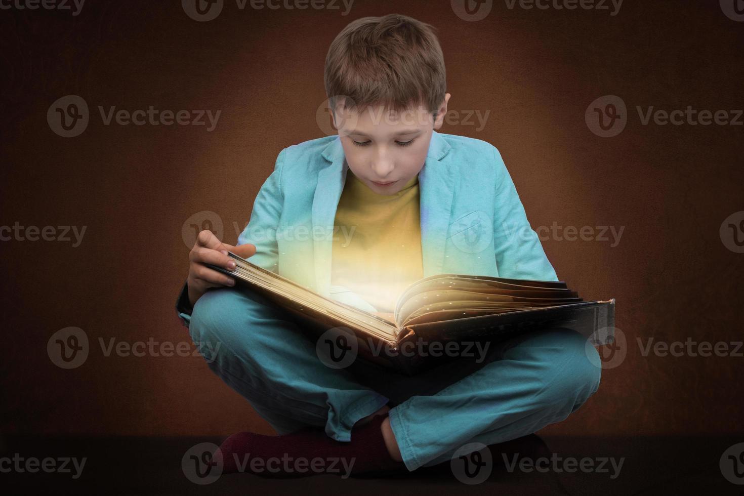 de jongen is lezing een boek met een magisch gloed. foto