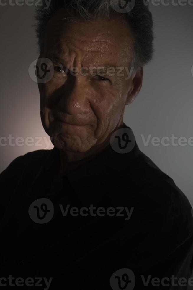 donker humeurig portret van een ouder Mens in laag licht vervelend een zwart overhemd foto