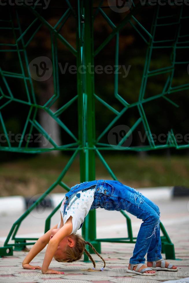 een weinig meisje maakt een brug, buigen haar terug in straat . een flexibel kind, aan het doen gymnastiek opdrachten. foto