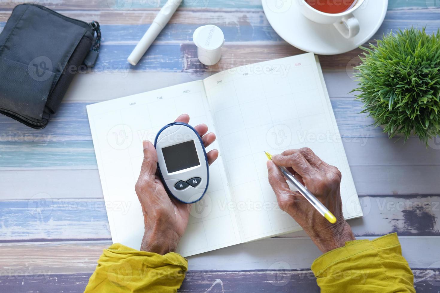 senior vrouw met glucosemeter en schrijven in een planner foto