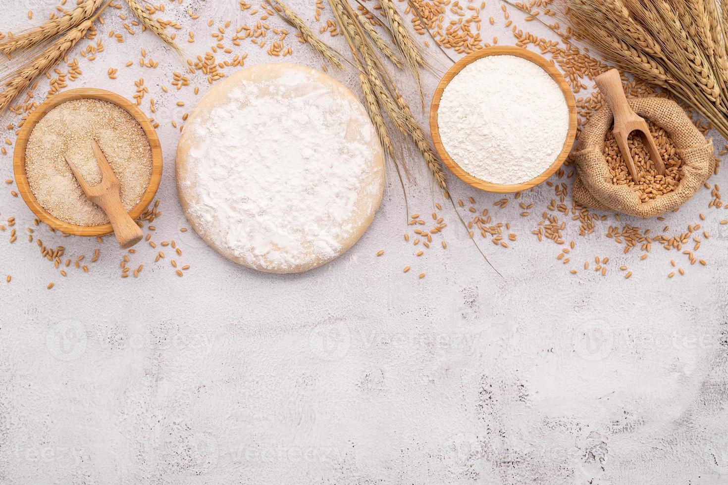 de ingrediënten voor zelfgemaakte pizzadeeg met tarweoren, tarwemeel en tarwekorrels opgezet op een witte betonnen achtergrond. foto