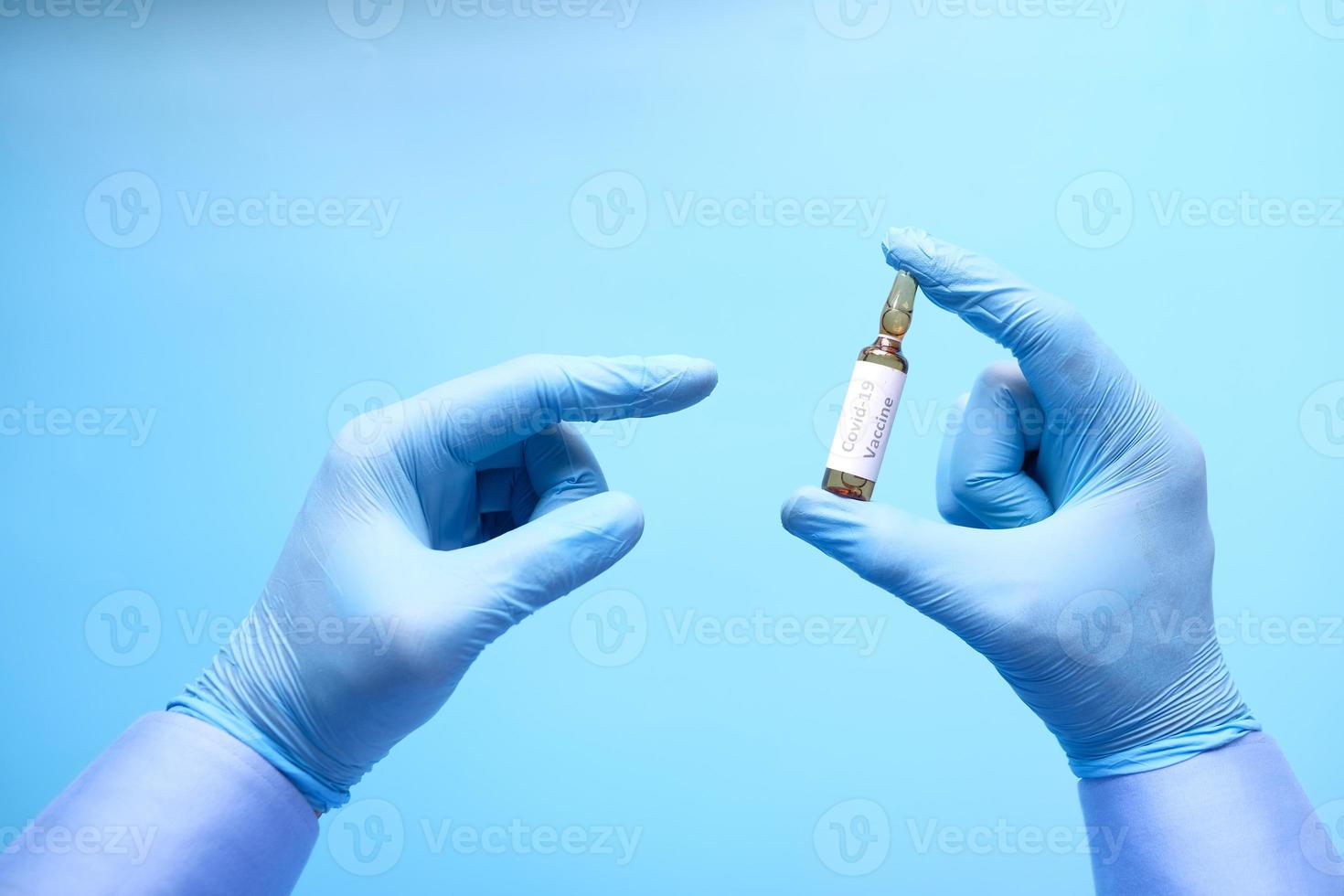 dien latexhandschoenen in met covid-19-vaccin op blauwe achtergrond foto