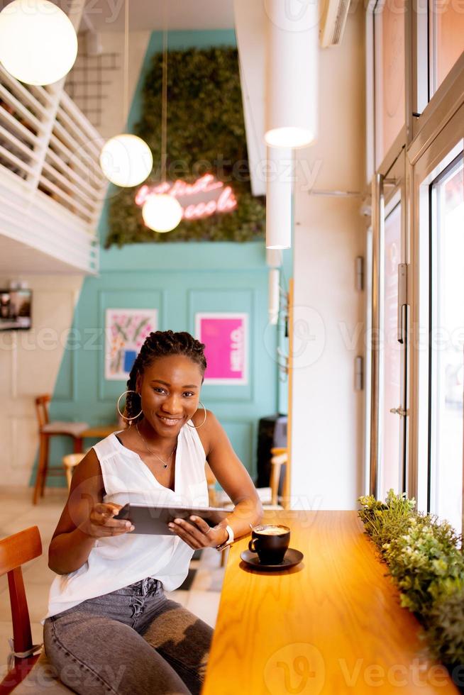 jong zwart vrouw drinken koffie terwijl op zoek Bij digitaal tablet in de cafe foto