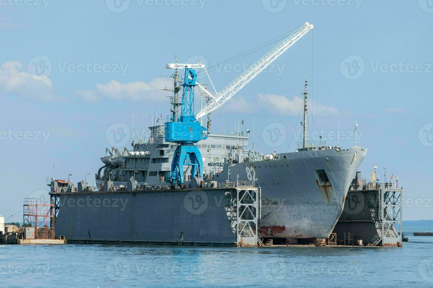 grote ijzeren marineschepen in scheepswerf voor reparatie. grote kraan in de werf. blauwe zee haven foto