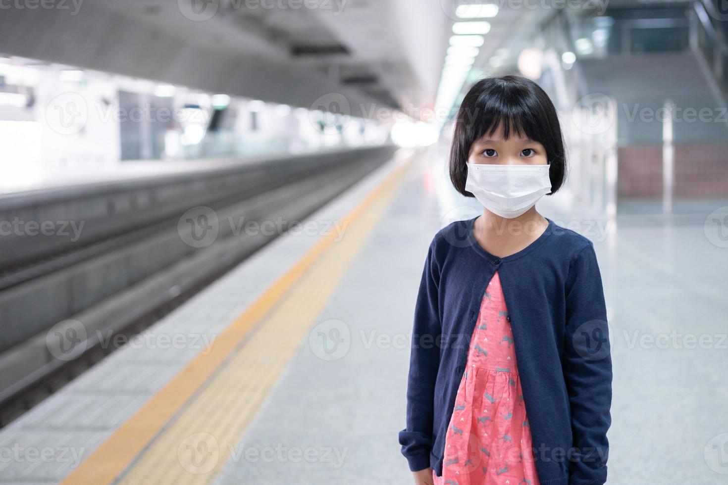 klein meisje met chirurgisch masker gezichtsbescherming griep en virusuitbraak in de skytrain of metro van het openbaar vervoer. concept van nieuwe normale levensstijl, met het openbaar vervoer om naar school te reizen. foto