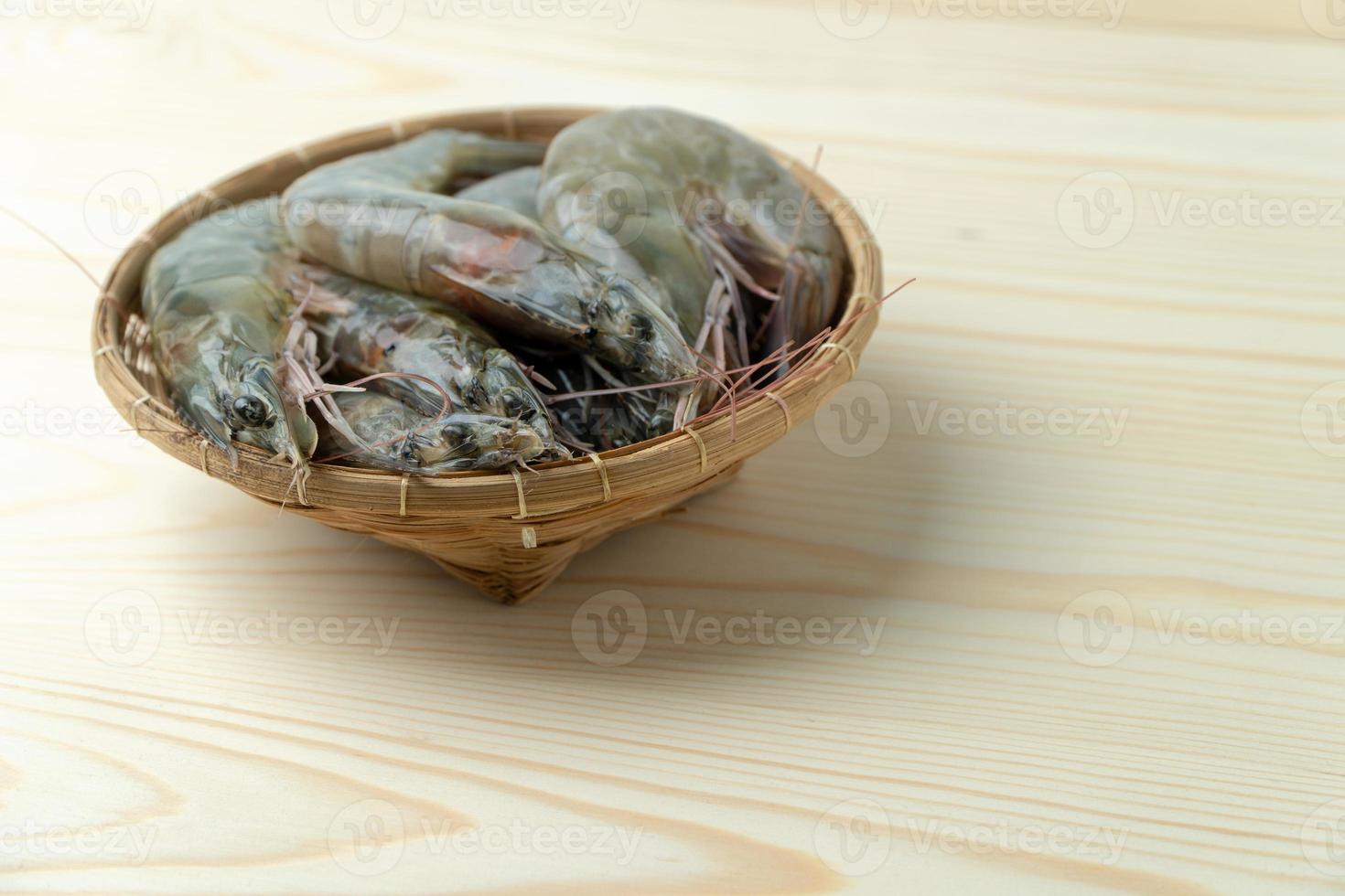 dichtbij omhoog groep van vers rauw grote Oceaan wit garnaal in bamboe kom Aan houten tafel. foto