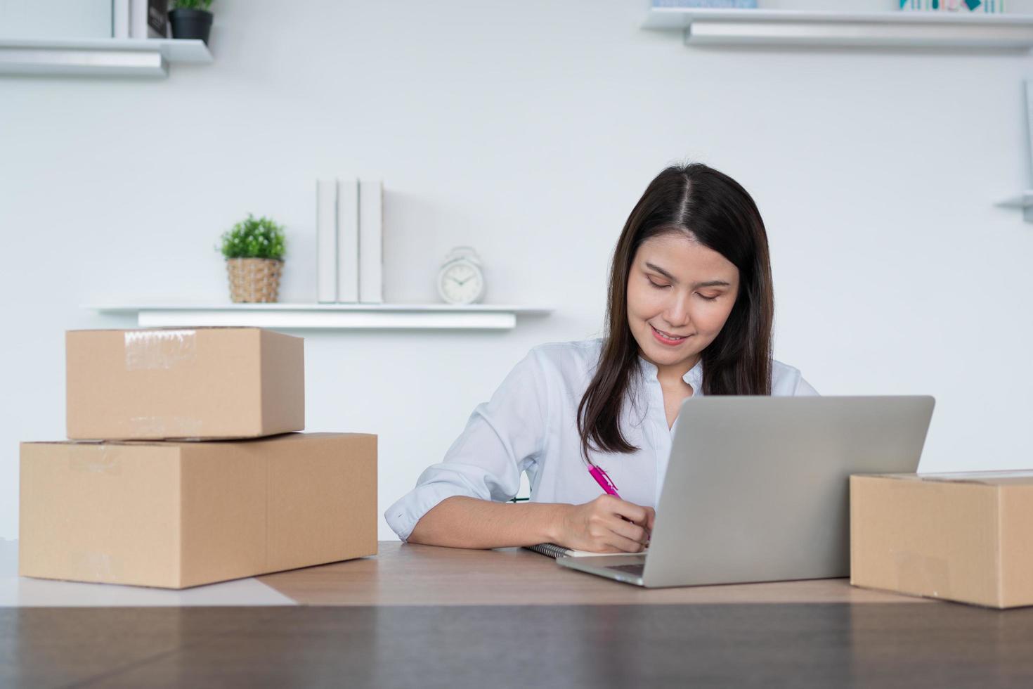 gelukkig jong Aziatisch vrouw ondernemer, nemen Notitie na controleren bestellen en glimlach voor uitverkoop succes van online boodschappen doen op te slaan, concept van de handelaar, klein bedrijf, online bedrijf, en e-commerce. foto