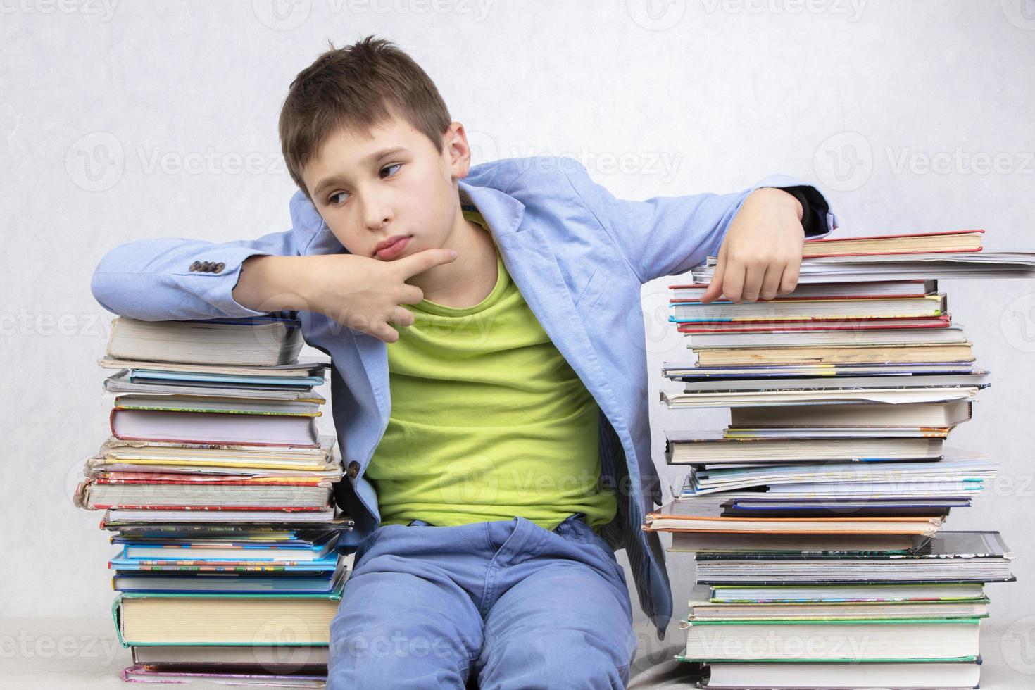 verdrietig nadenkend jongen leerling zit tussen stapels van boeken. verkrijgen kennis. moe leerling. foto