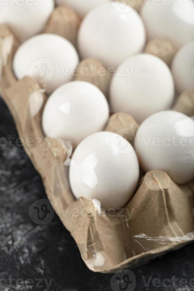 rauwe kippeneieren in een eierdoos op een marmeren achtergrond foto