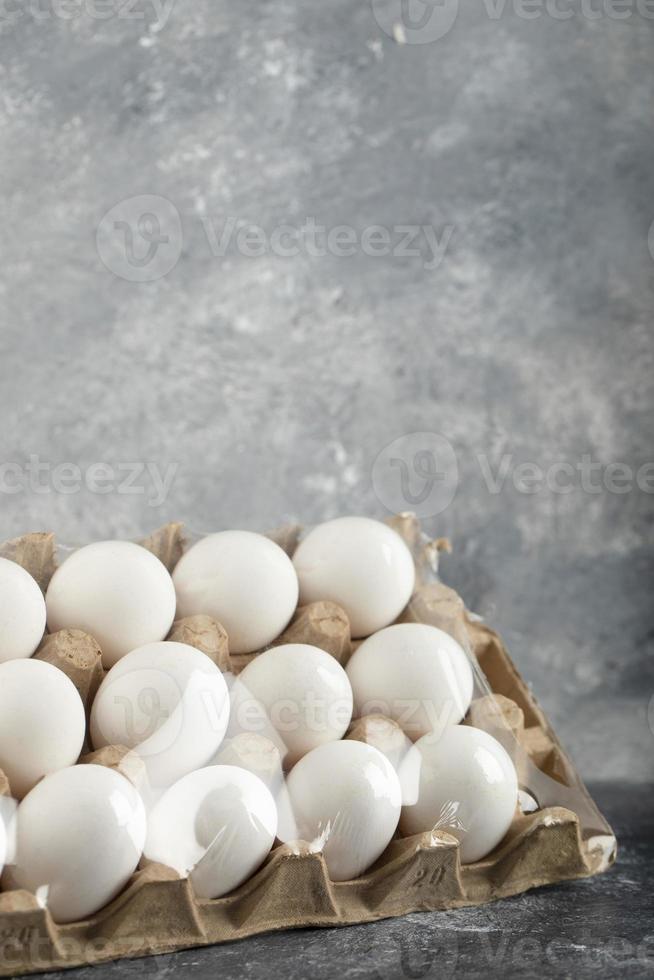 rauwe kippeneieren in een eierdoos op een marmeren achtergrond foto