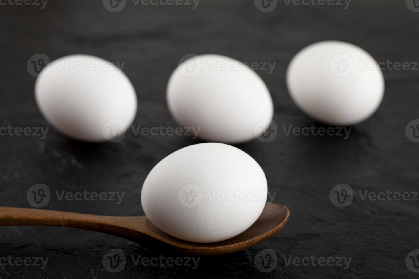 rauwe witte eieren en een houten lepel op een zwarte achtergrond foto