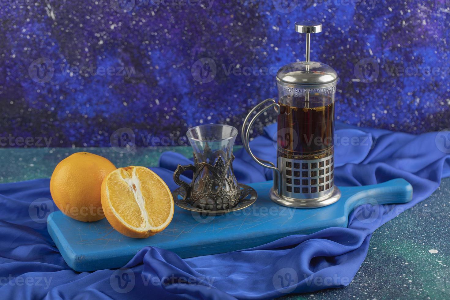 glas thee, sinaasappel en theepot op een blauw bord foto