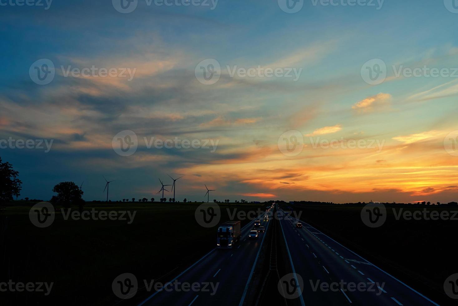 snelweg met auto verkeer en windmolen turbines Bij zonsondergang foto