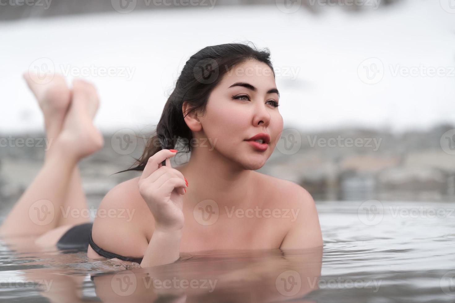 vol dacht jong model- in zwart het baden zwempak aan het liegen naar beneden Aan maag in zwembad balneotherapie spa foto