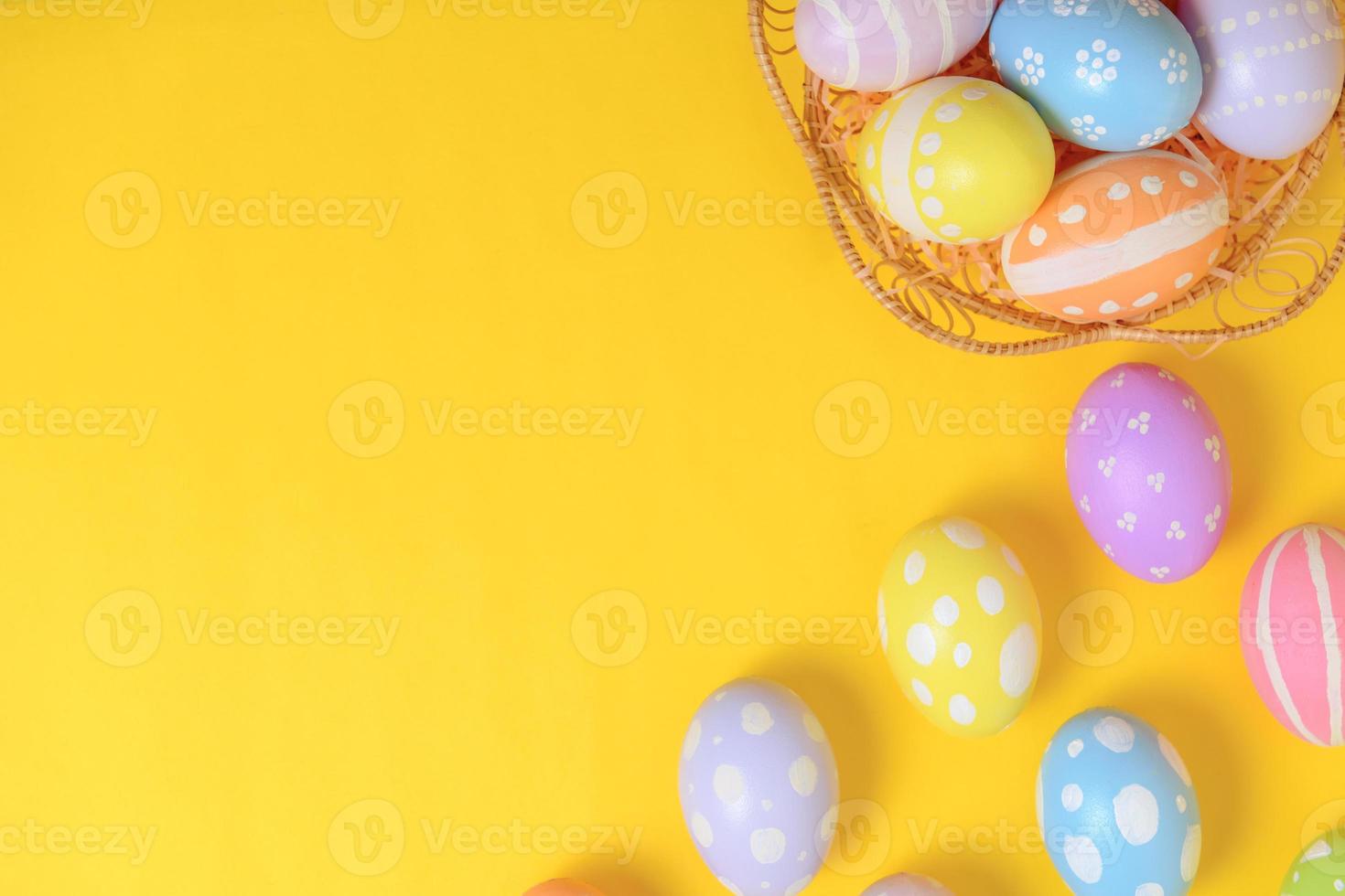 gelukkig Pasen viering vakantie. kleurrijk pastel geschilderd eieren in rieten mand nest decoratie Aan een geel achtergrond. seizoensgebonden groet geschenk kaart concept. top visie, vlak leggen, kopiëren ruimte. foto