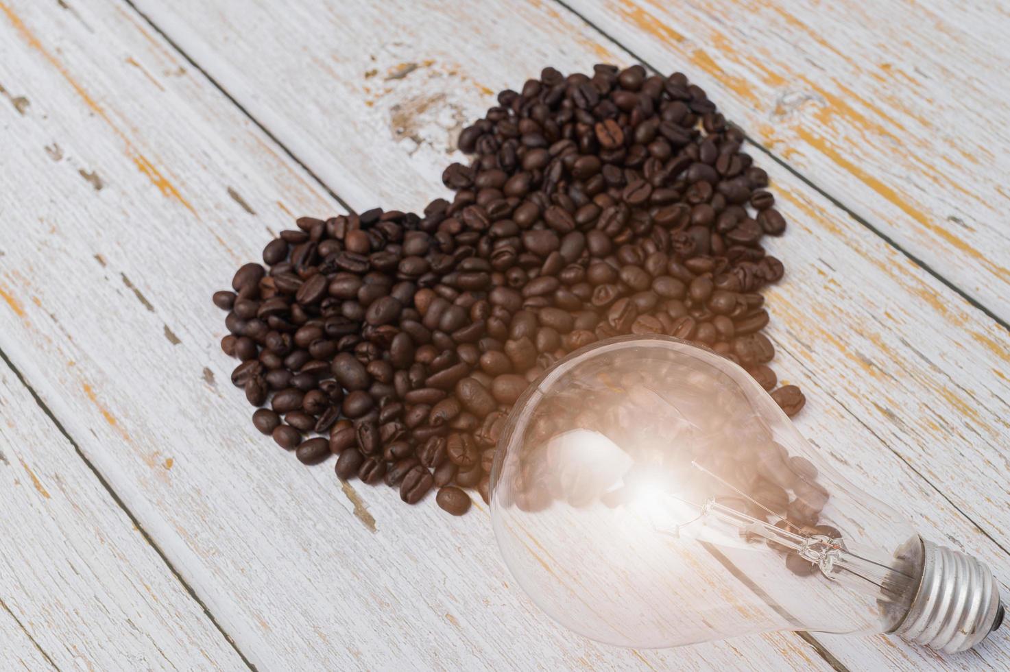 koffiebonen in hartvorm en een gloeilamp op een houten tafel foto
