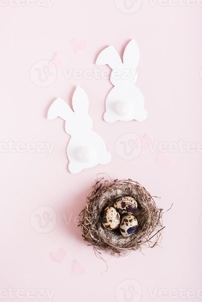 gelukkig Pasen paar van wit konijnen en kwartel eieren in nest Aan roze achtergrond top en verical visie foto
