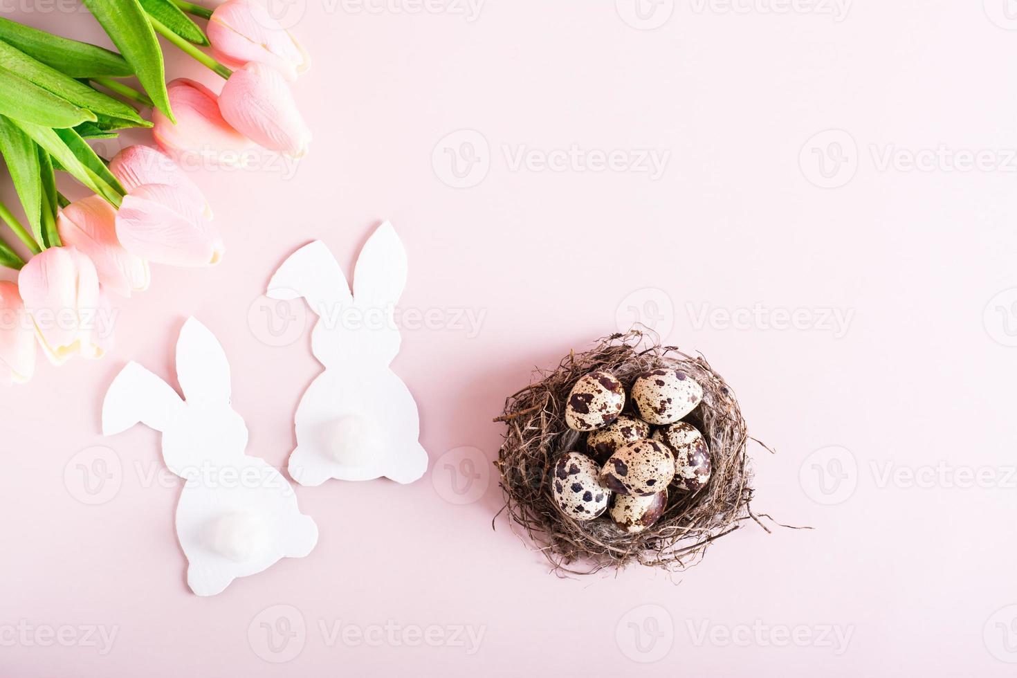 gelukkig Pasen paar van wit konijnen, kwartel eieren in nest en bloemen Aan roze achtergrond top visie foto