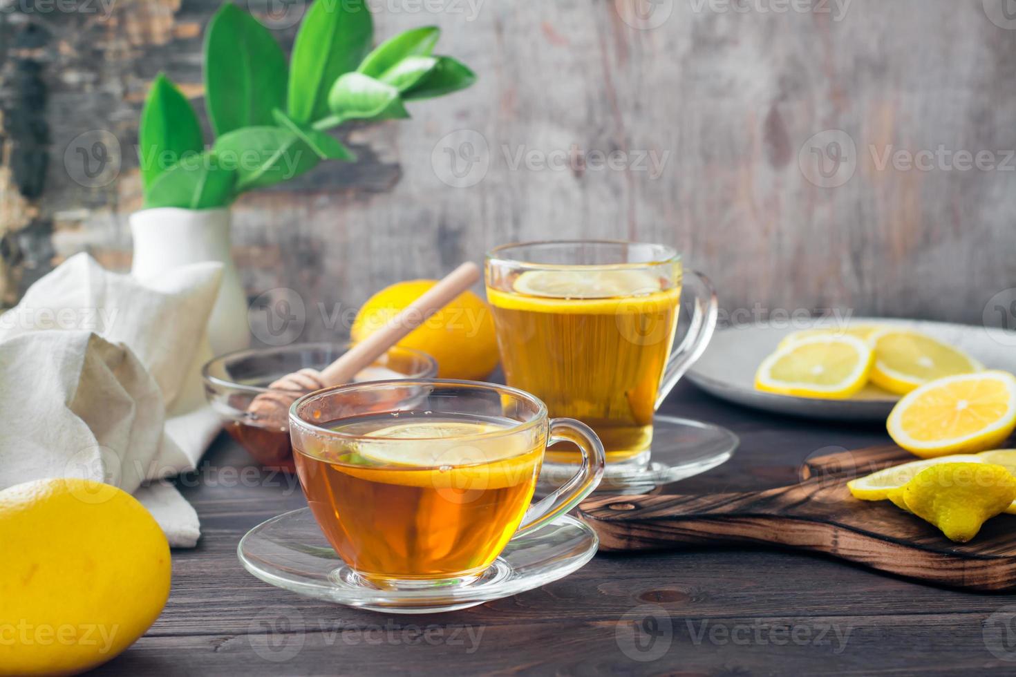 twee cups van thee met citroen, een gesneden citroen en een kom van honing Aan een houten tafel. vitamine opwarming drinken foto